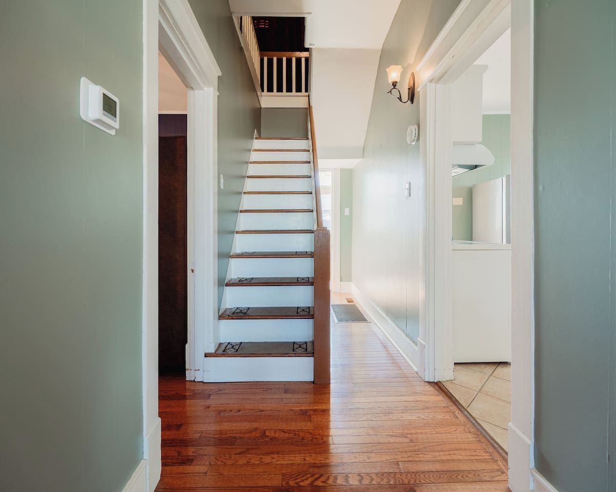 Un escalier avec des marches en bois menant à un palier, une porte blanche et un couloir avec un interrupteur sur le mur.