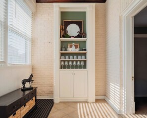 A room with a white brick wall, a white cabinet with shelves, a black bench, and a patterned rug. - Historic 4 bedroom home (Russellville)