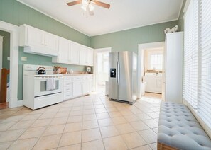 A spacious kitchen with white cabinets, a stainless steel refrigerator, and a tiled floor.