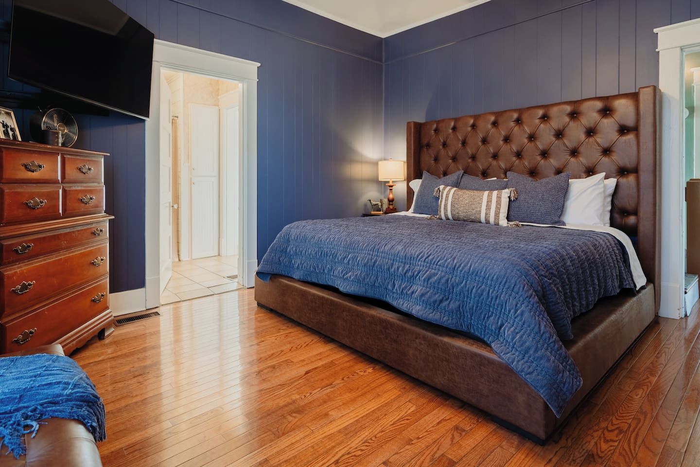 A bedroom with a large bed, wooden dresser, and a television.