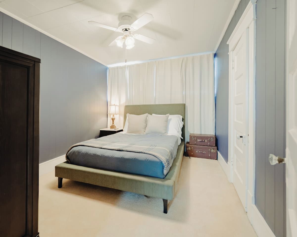 A bedroom with a bed, a ceiling fan, a nightstand, and a lamp.