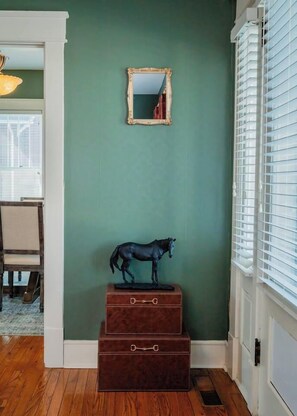 Ein Zimmer mit grüner Wand, einem Spiegel, einer hölzernen Kommode und einer Pferdestatue.