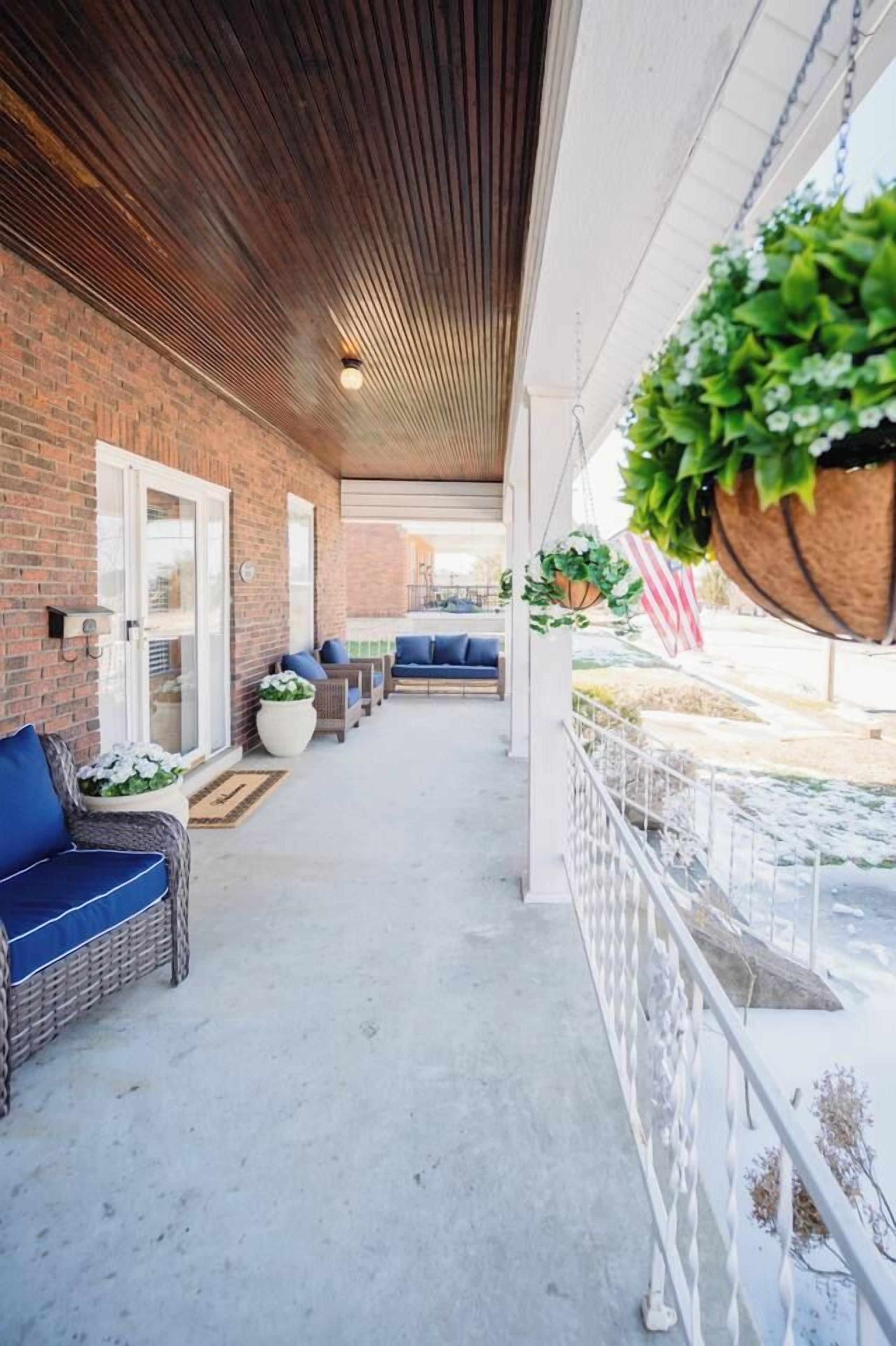 A covered outdoor area with a brick wall, wicker furniture, and hanging plants.