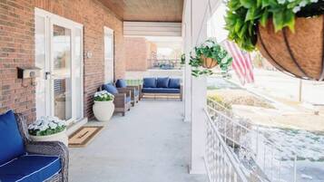 A covered outdoor area with a brick wall, wicker furniture, and hanging plants.