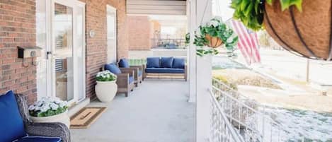 A covered outdoor area with a brick wall, wicker furniture, and hanging plants.