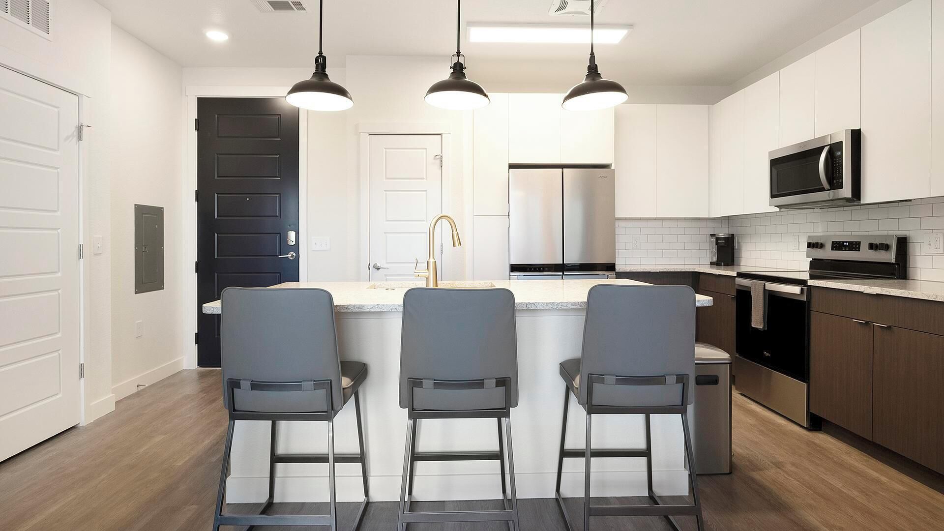 Una cocina moderna con una isla central, taburetes de bar, electrodomésticos de acero inoxidable e iluminación colgante.