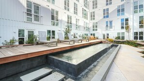 A modern building with a rooftop pool area, including lounge chairs and a wooden deck. - Landing | Stylish 2BD, Yoga Studio, Gym (Durham)