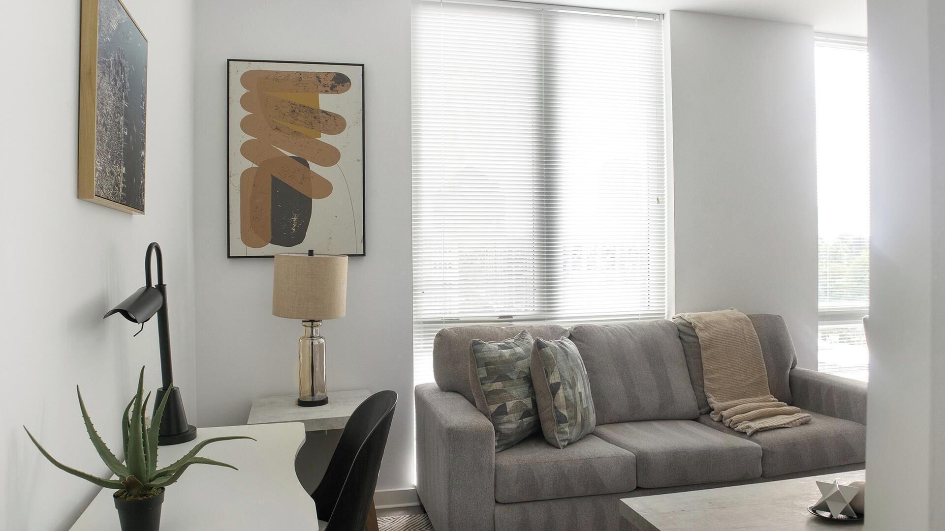 Un salon avec un canapé gris, une lampe, une plante et des œuvres d’art accrochées au mur.