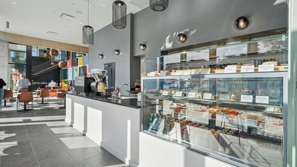 A modern cafe with a glass display case of pastries and a coffee machine. - Landing | Amazing 1BD, Yoga Studio, Gym (Durham)