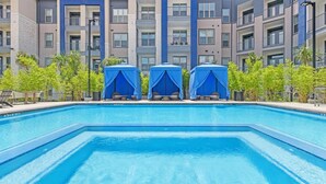 Une piscine dotée de trois espaces de repos abrités et, en arrière-plan, un immeuble à plusieurs étages.