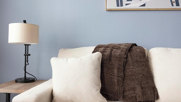 Une pièce avec un canapé blanc, un plaid marron et un lampadaire.