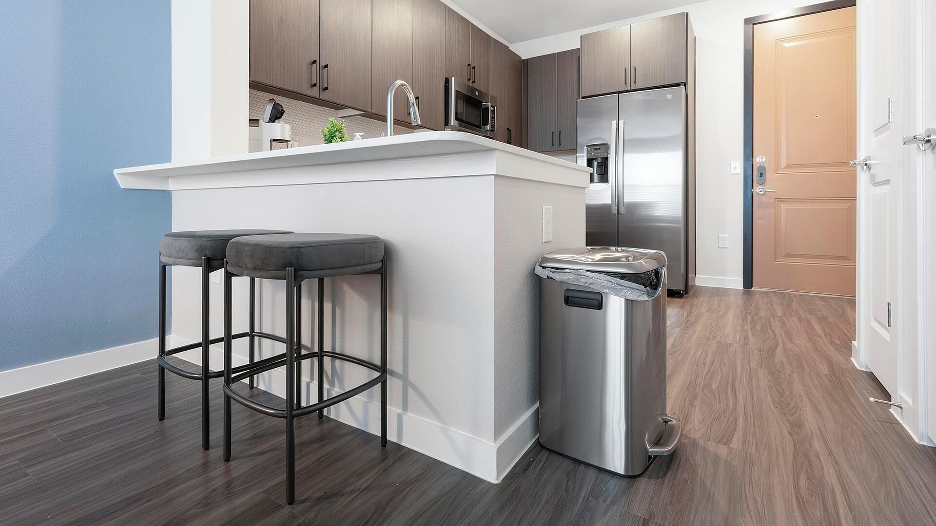 A modern kitchen with dark wood cabinets, a stainless steel refrigerator, and a white countertop.