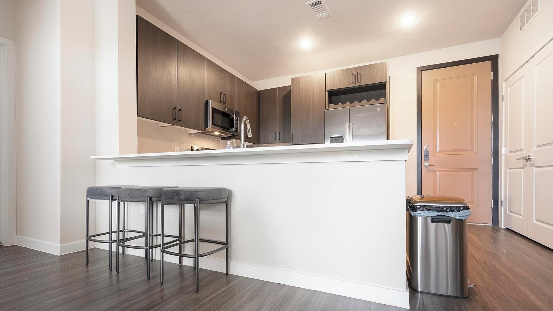 A modern kitchen with a central island, bar stools, and a trash bin.