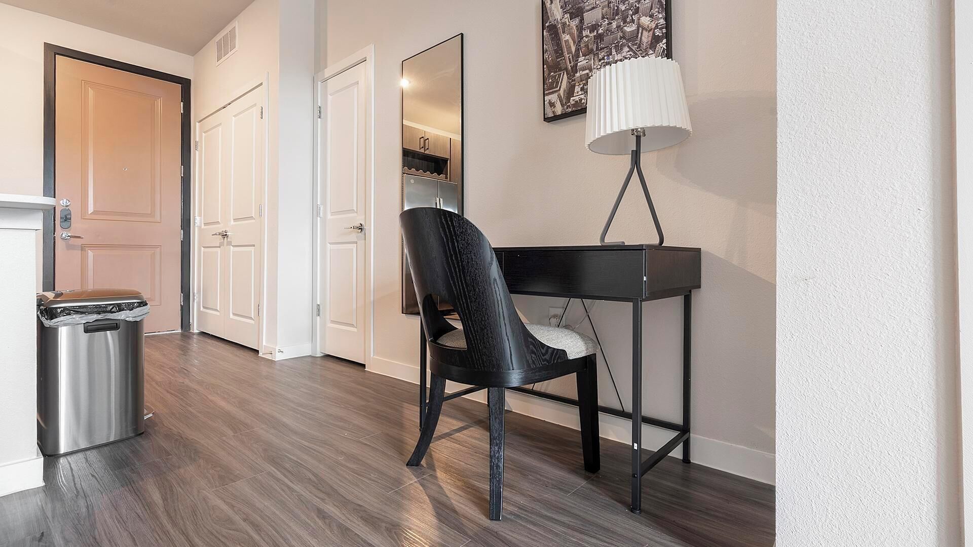 A hallway with a trash bin, a chair, a table, and a lamp.