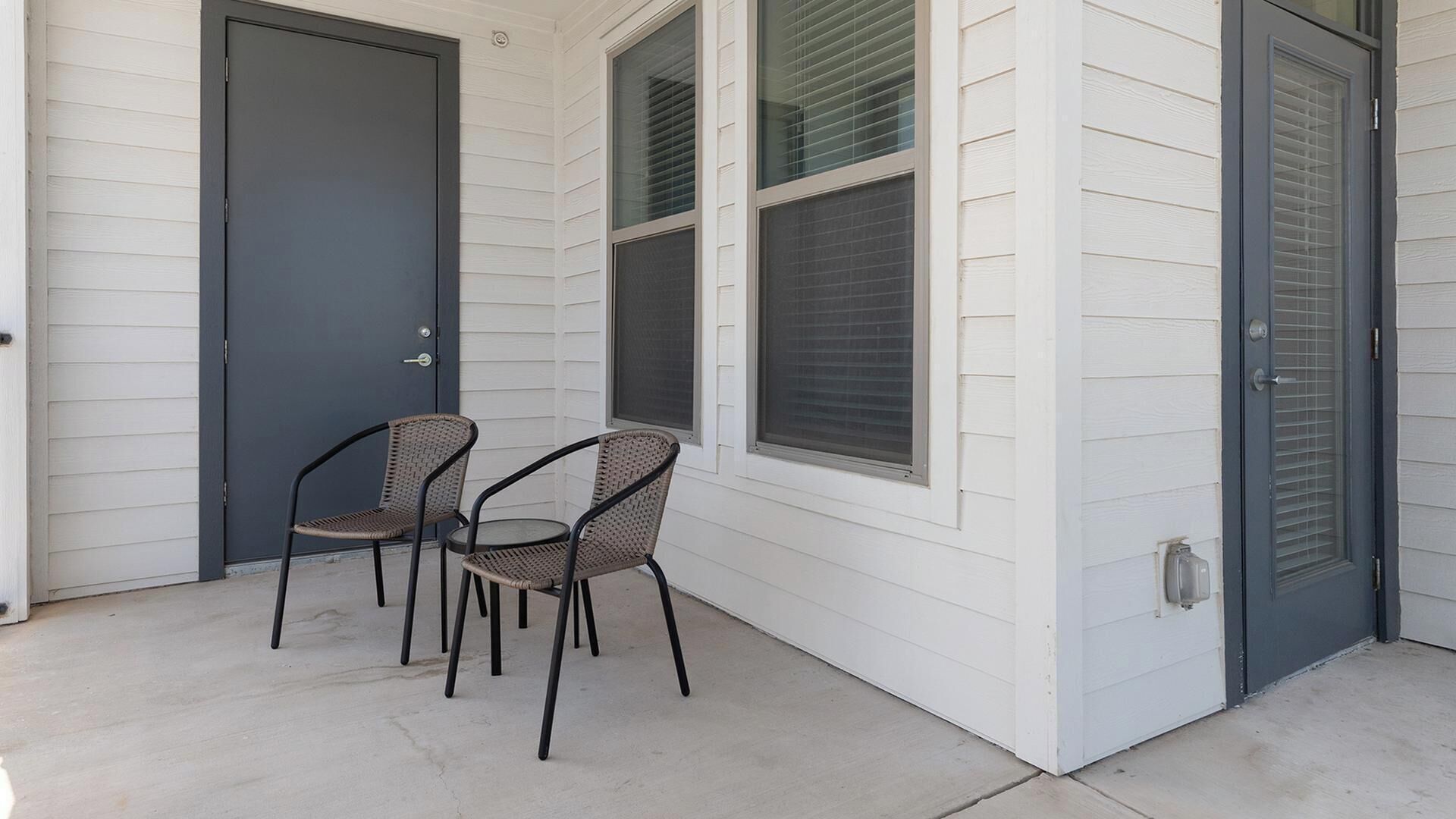 A covered porch with two wicker chairs and a dark door.