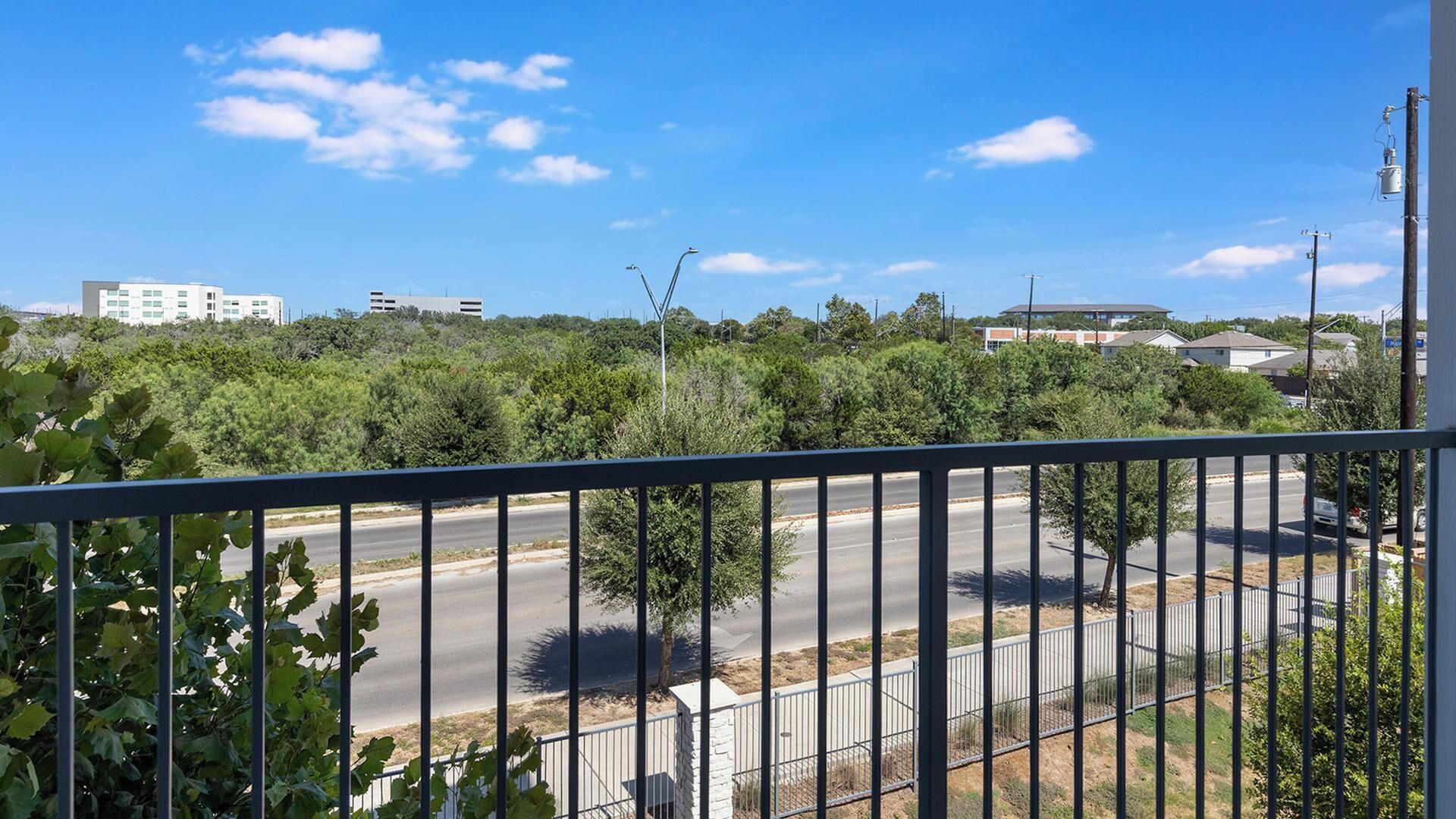 Un balcone con vista su una strada, del verde e edifici in lontananza.