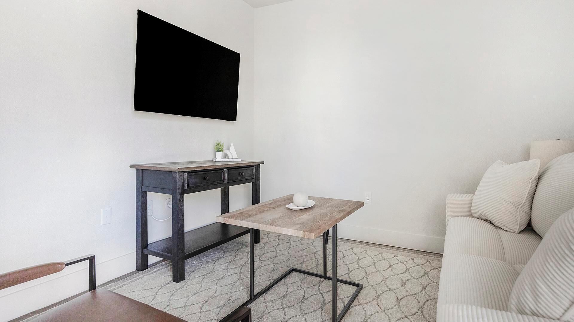 Una sala de estar moderna con una mesa de madera oscura, un sofá blanco y un televisor montado.