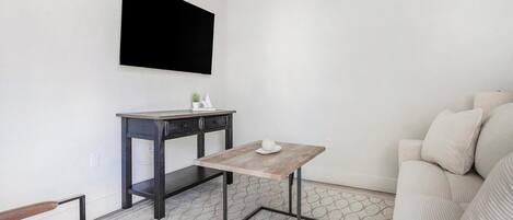 Una sala de estar moderna con una mesa de madera oscura, un sofá blanco y un televisor montado.