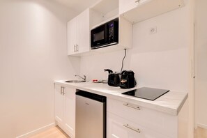 A compact kitchen with white cabinets, a microwave, a coffee maker, and a dishwasher.