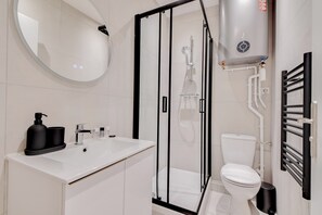 A modern bathroom with a glass-enclosed shower, a white sink with black soap dispensers, and a toilet with a black trash bin.
