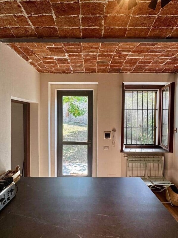 A room with a brick ceiling, a large window with metal bars, a radiator, and a table. - Independent Home with Private Courtyard - Monferrato (Montemagno)