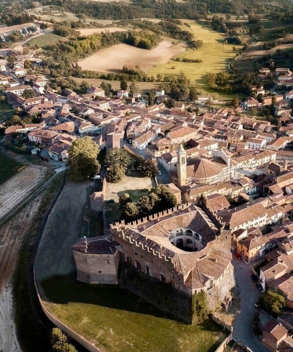 Vista aérea de un pueblo histórico con una imponente estructura que recuerda a un castillo, rodeado de viviendas y campos abiertos.