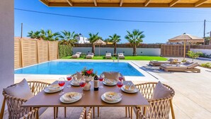 A poolside dining area with a table set for six, overlooking a swimming pool. - Villa Kamelia Seaside Almyra by Villa Plus (Agkisaras)