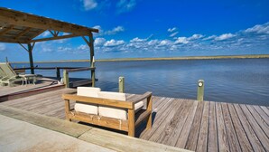 Une terrasse en bois avec un banc et des chaises longues, donnant sur une étendue d’eau calme.