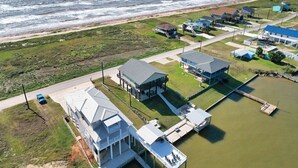 Vue aérienne d’une propriété située sur la côte, comprenant plusieurs bâtiments, un quai et une route menant à la plage.