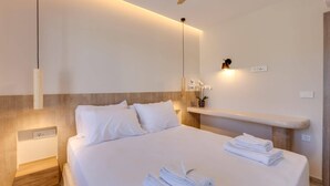 Ett modernt hotellrum med en stor säng, ett sängbord, en väggmonterad lampa och en liten hylla med en vas med blommor.