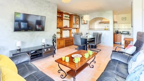 A living room with a TV, a dining table with chairs, a sofa, and a kitchen area with a microwave. - Villa Juan by Villa Plus (Cala d'Or)