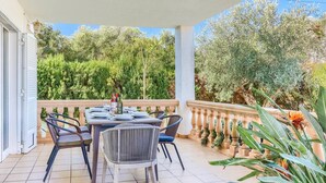 A covered outdoor dining area with a table set for four, surrounded by wicker chairs. - Villa Juan by Villa Plus (Cala d'Or)