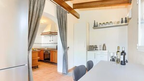 A modern kitchen with a dining area, featuring a white cabinet, a hanging shelf with bottles, and a table with chairs. - Villa Juan by Villa Plus (Cala d'Or)
