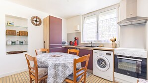 A compact kitchen with a washing machine, oven, and dining area with chairs and a table. - Apartment in Saint-Pierre-d’Oléron with Private Terrace, Garden, and Wi-Fi (Saint-Pierre-d'Oléron)