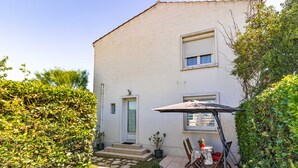 A two-story building with a patio area featuring a table and chairs, potted plants, and a door. - Apartment in Saint-Pierre-d’Oléron with Private Terrace, Garden, and Wi-Fi (Saint-Pierre-d'Oléron)