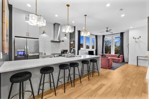 Een moderne keuken met een groot eiland, barkrukken, roestvrijstalen apparatuur en hanglampen.