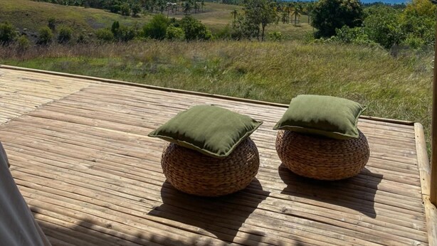 Une terrasse en bois agrémentée de deux coussins ronds en fibres tressées, offrant une vue sur un paysage côtier sous un ciel dégagé.