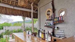 Un espace bar avec un comptoir en bois, des chaises en osier et des étagères remplies de bouteilles et de verres.
