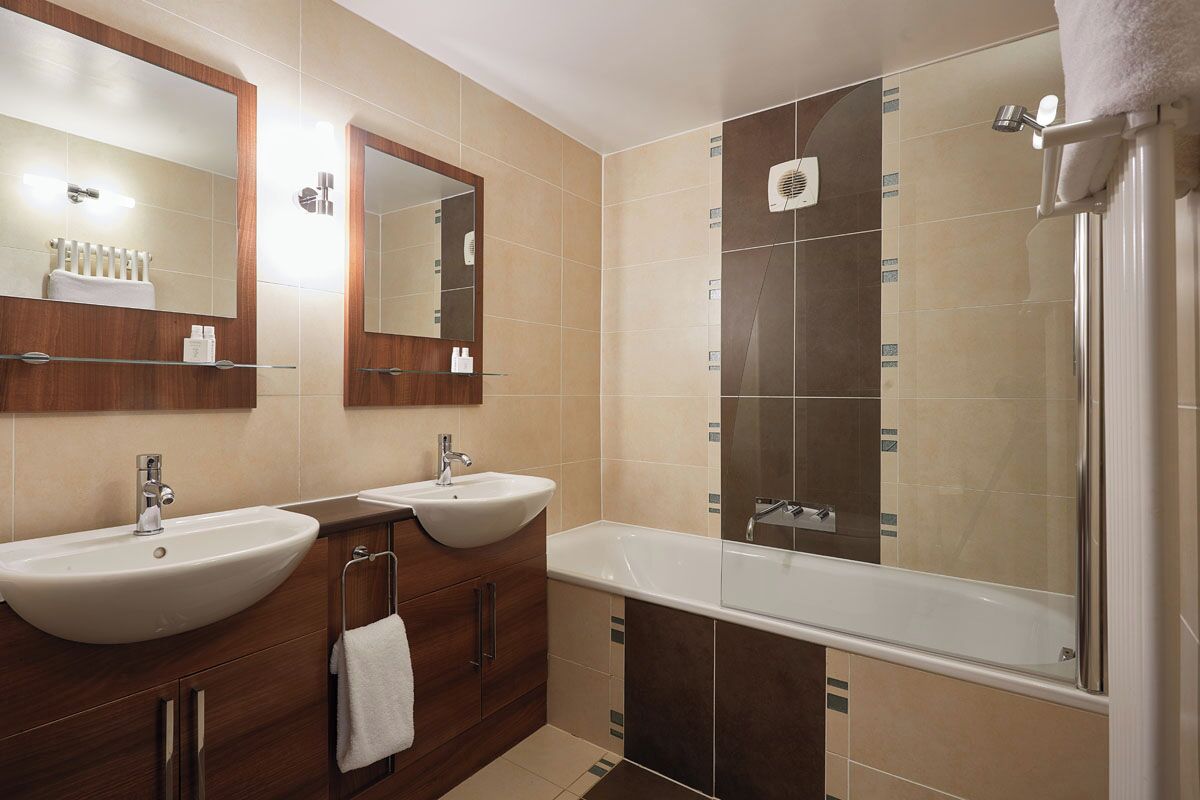 Un baño moderno con dos lavamanos, una bañera y una ducha.