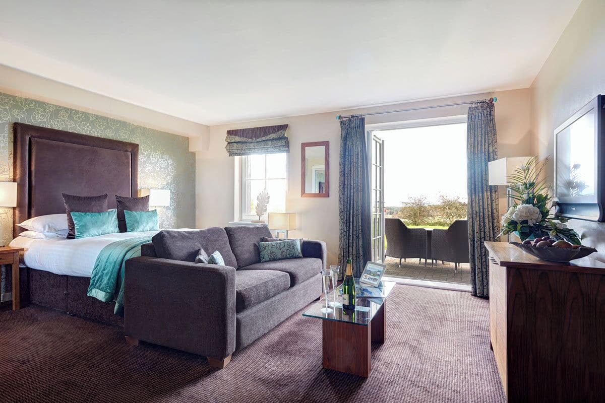 A hotel room with a bed, sofa, and a dining area with a table and chairs.