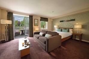 A hotel room with a bed, a sofa, a glass coffee table, and a view of a balcony. - Landal Whitbarrow (Penrith)