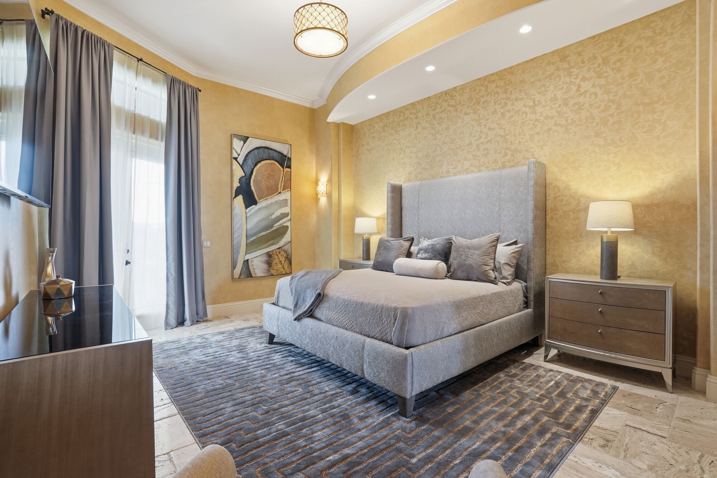 A modern bedroom with a large bed, bedside lamps, a nightstand, and a decorative painting on the wall.