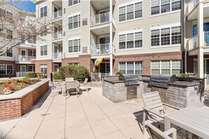 A multi-story residential building with a patio area featuring outdoor seating and a barbecue grill.