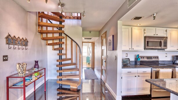 A modern kitchen with white cabinets, stainless steel appliances, and a wooden staircase. - The Intercoastal #209 - Intercoastal Escape (Indian Shores)