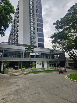 A modern building with a large glass facade, a visible logo, and a paved entrance area with steps.