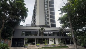 Un edificio moderno con una amplia entrada de vidrio, rodeado de follaje y un edificio alto contiguo.