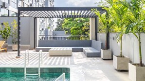 Zona de piscina en la azotea con pérgola, asientos y plantas en macetas.
