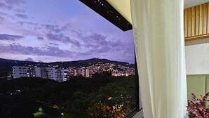 Un balcón con vistas a un paisaje urbano al anochecer, que incluye edificios y una colina en el fondo.