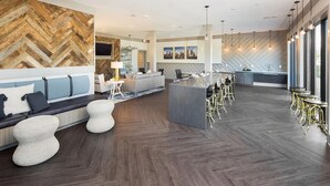 A modern hotel lobby with a herringbone wood wall, a seating area with sofas and chairs, a bar area with stools, and a large island with a bar counter. - Landing | Stylish 2BD, Yoga Studio, Gym (Charlotte)