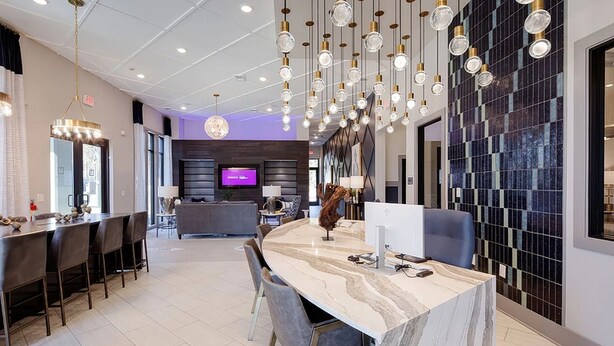 Un vestíbul d'hotel modern amb un taulell de recepció de marbre, una televisió de pantalla plana i una zona de bar.